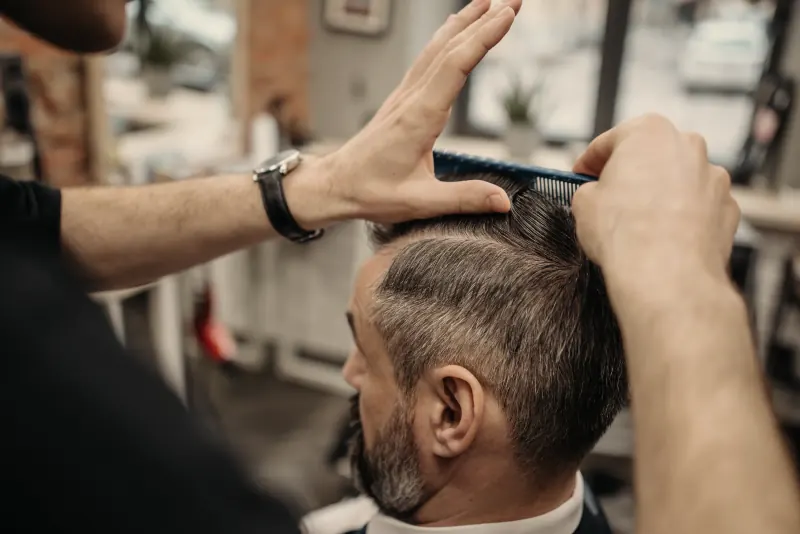 De kapper kamt het haar opzij en knipt de scheiding