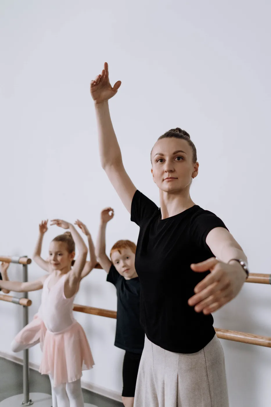 Een docent doet een armbeweging voor aan kleine balletdanseressen