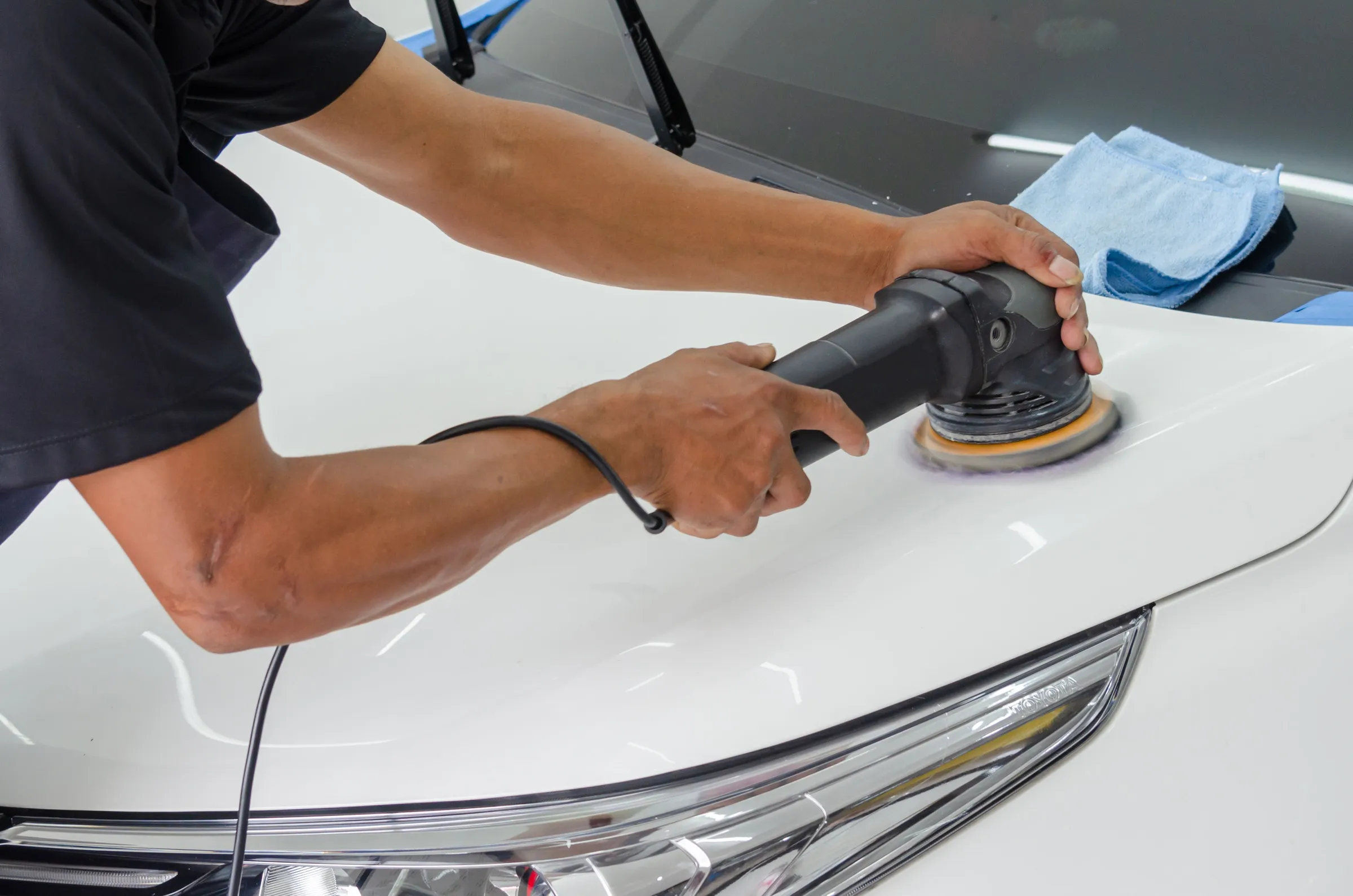 Een detailer polijst de motorkap van een witte auto