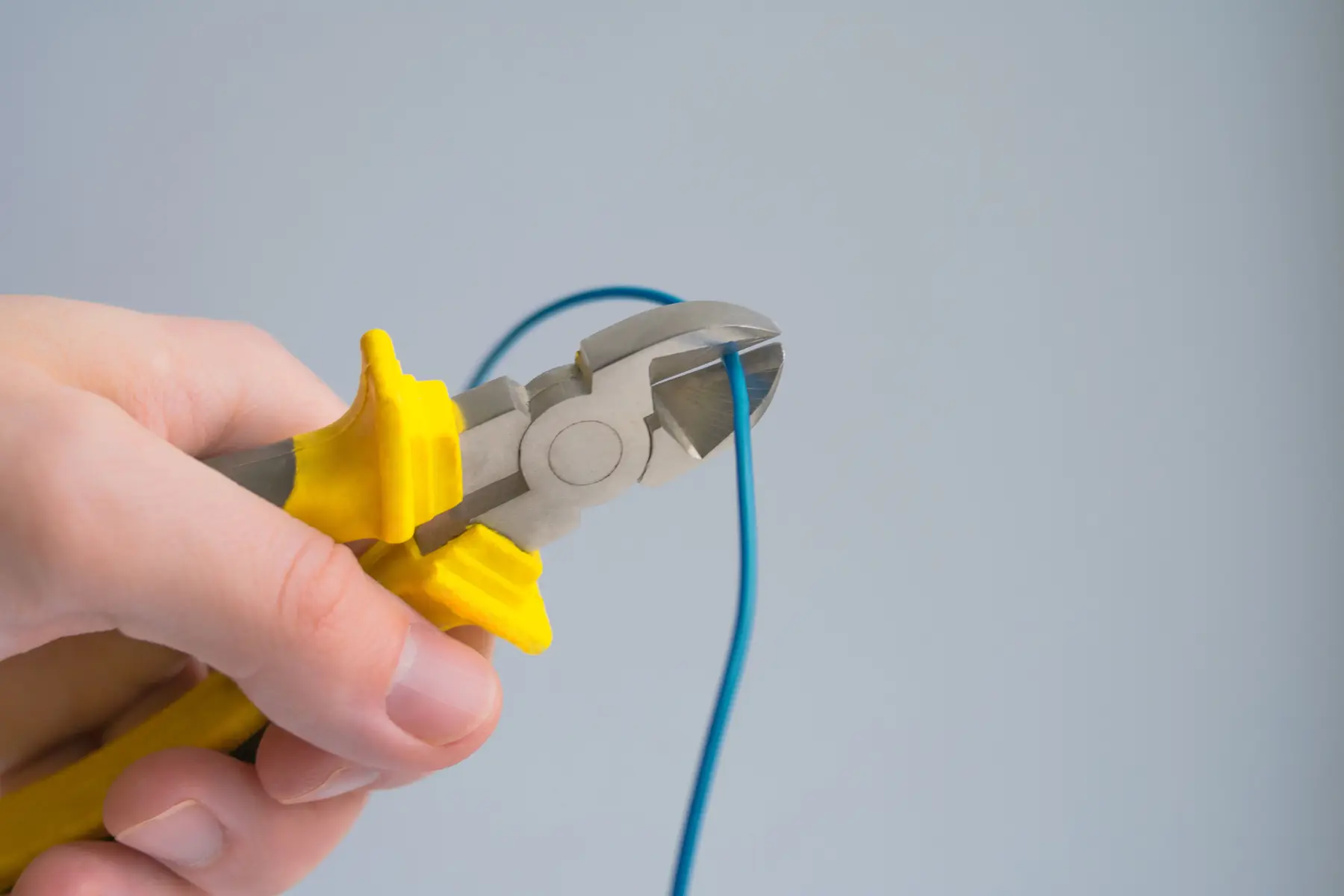 Een hand die met een kniptang met gele handgrepen een blauwe draad doorknipt