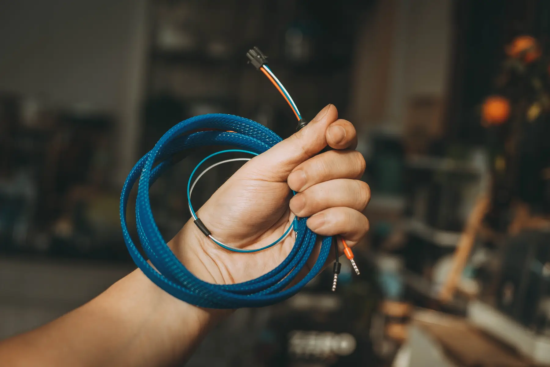 Een hand met een opgerolde blauwe gevlochten kabel in een werkplaats
