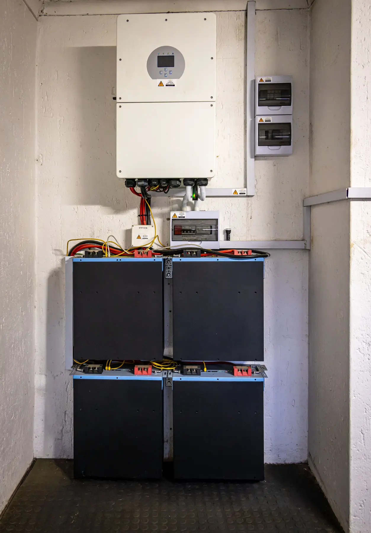 Een omvormer boven een accupakket in een technische ruimte met witte muren