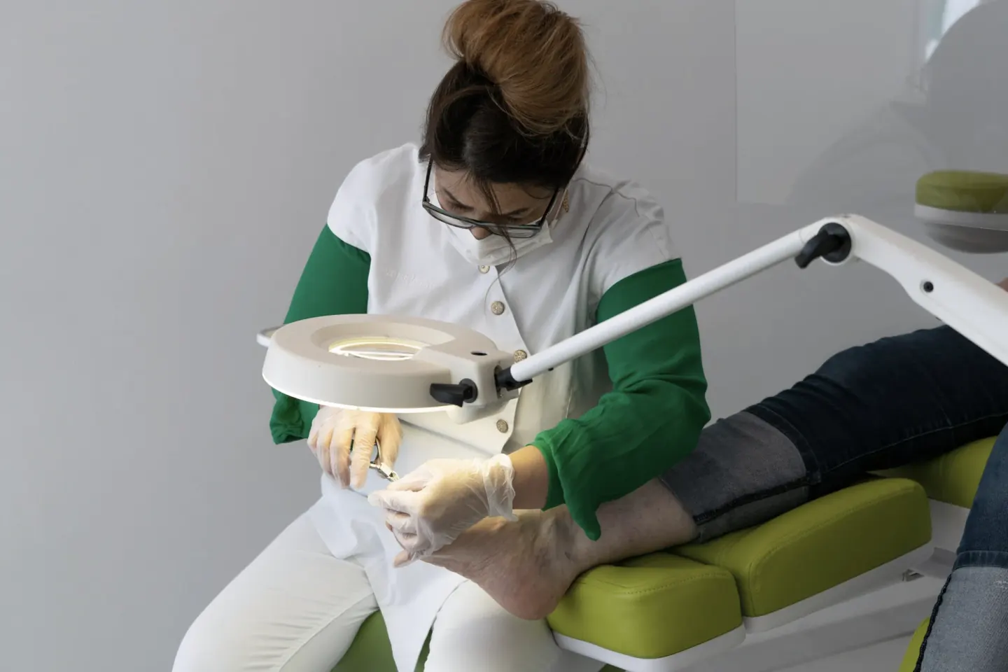 De medisch pedicure werkt onder een loeplamp aan de voet van een cliënt in de behandelstoel