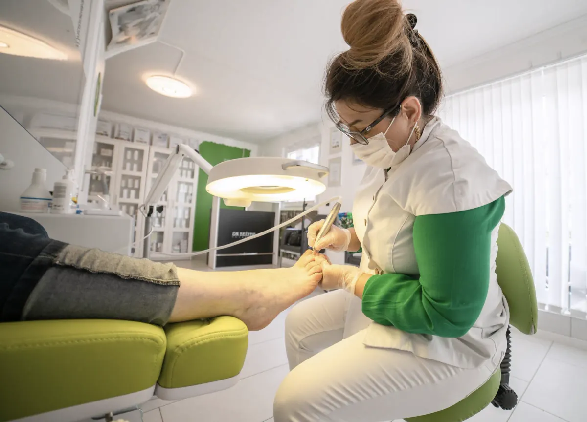 De pedicure verzorgt de voet van een cliënt onder de loeplamp, de cliënt ligt rustig achterover