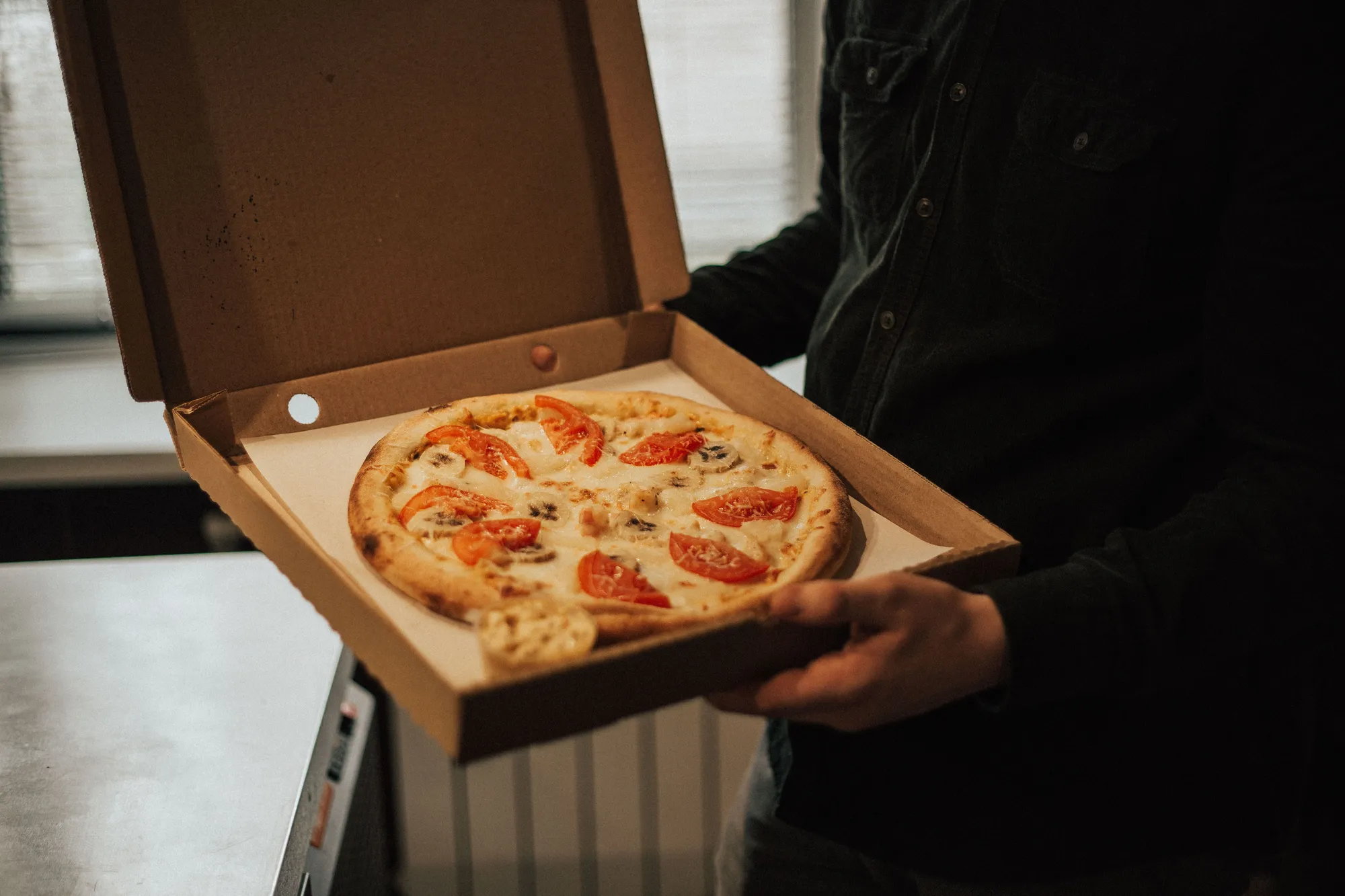 Iemand houdt een open pizzadoos met een tomatenpizza vast