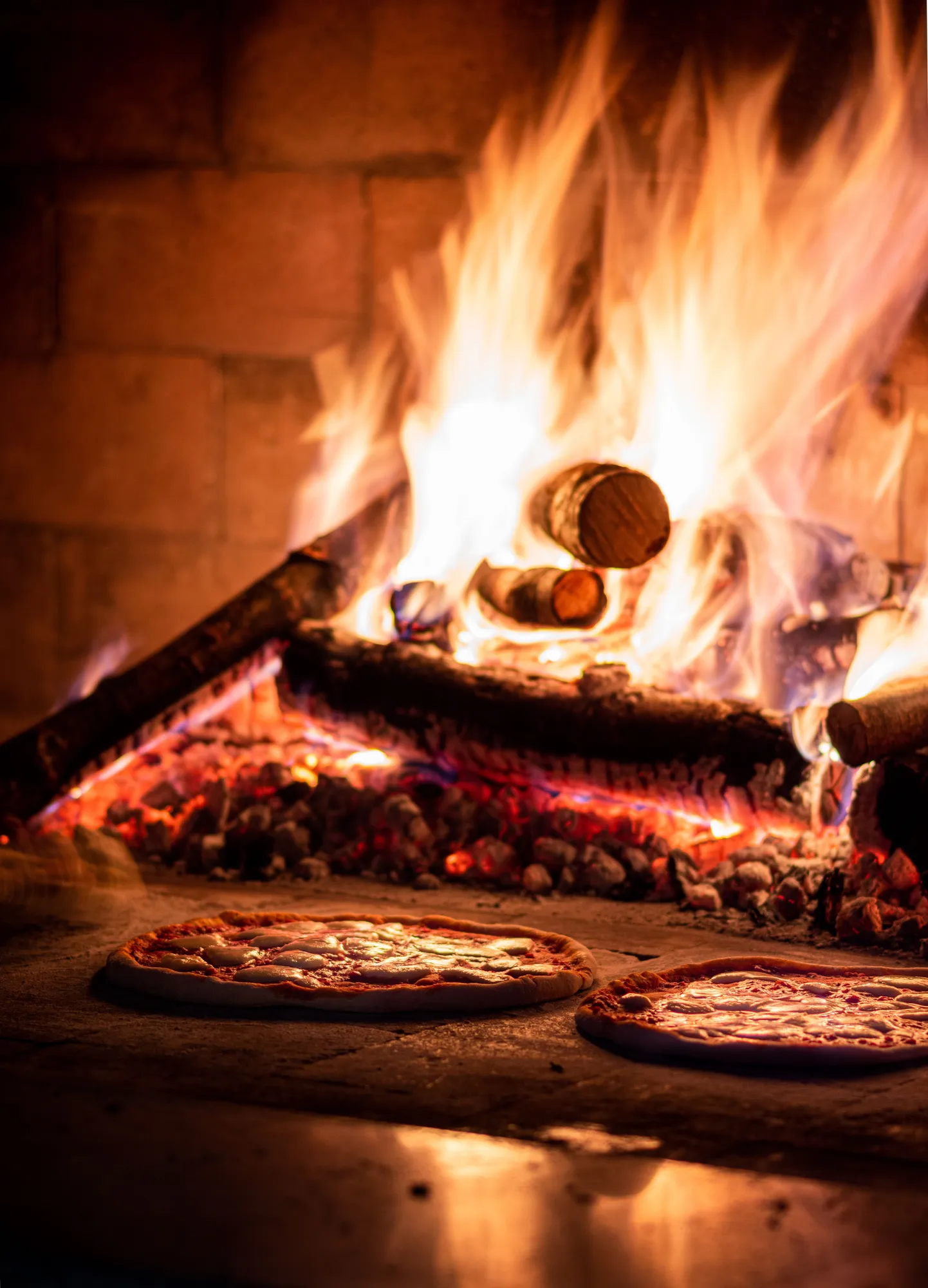 Pizza's in een stenen oven naast een houtvuur