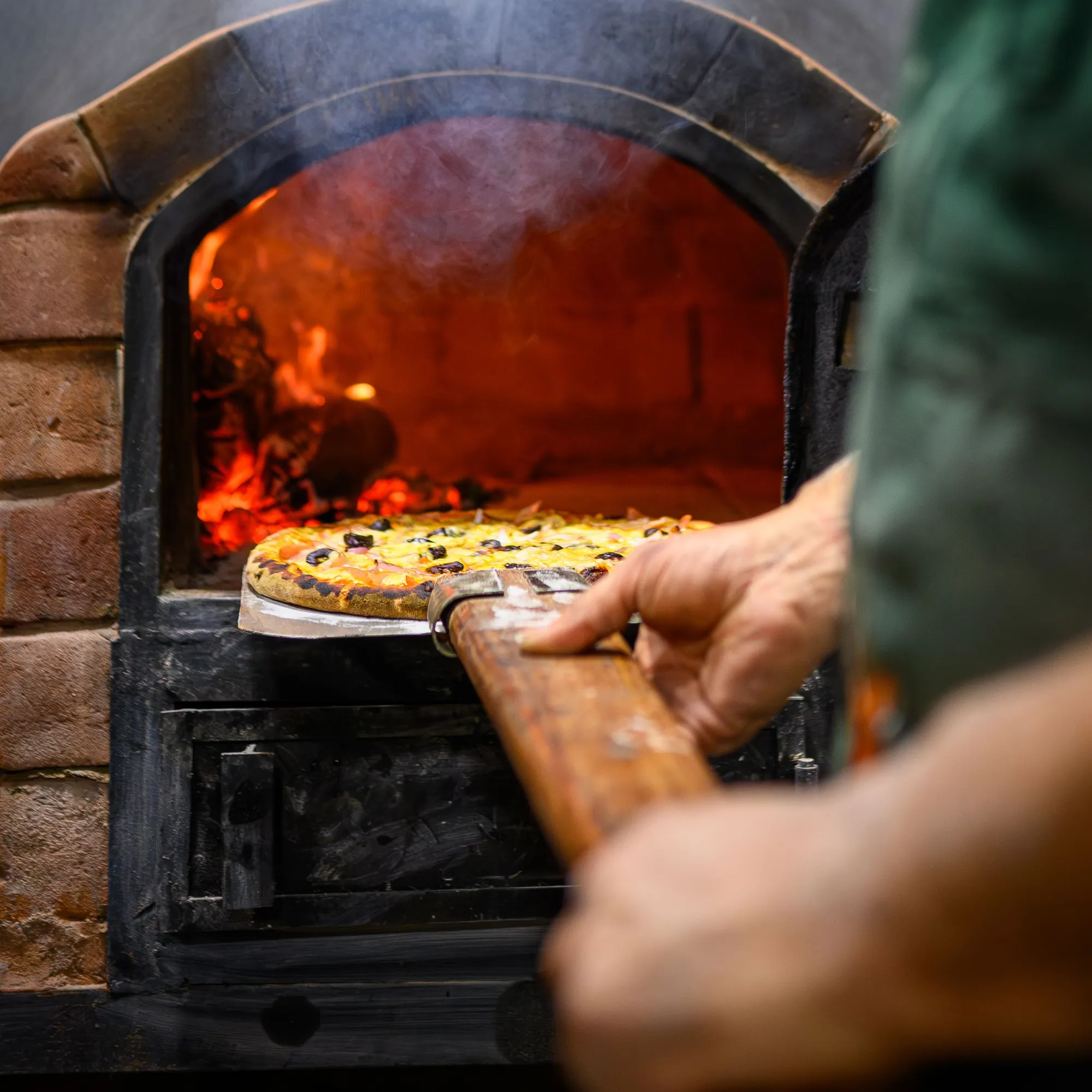 Een pizzaschep schuift een pizza in een stenen oven