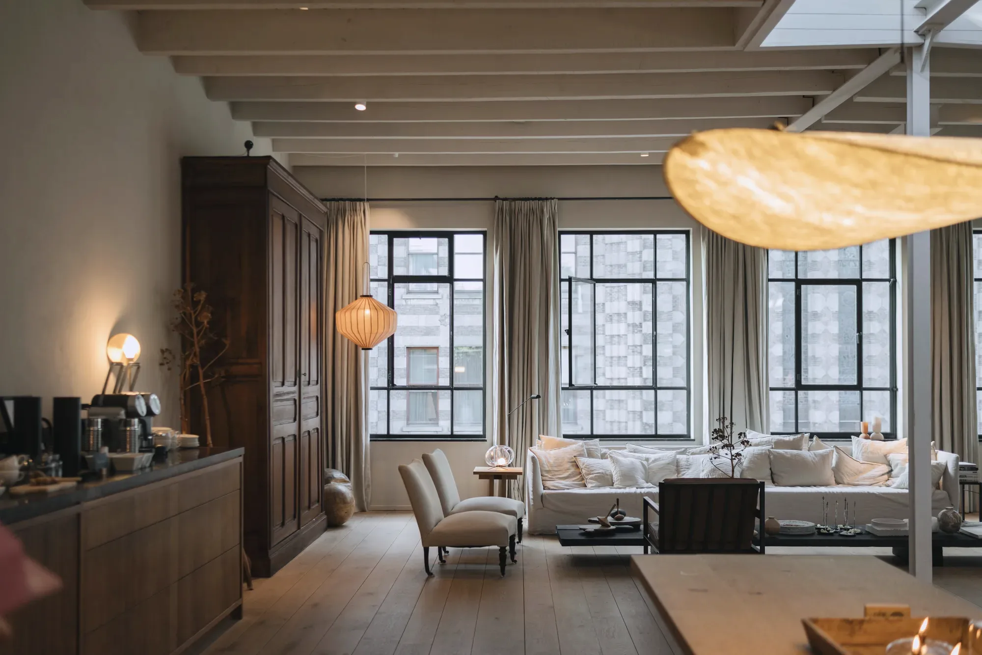 Een ruime woonkamer met hoge ramen, houten balken en een bank